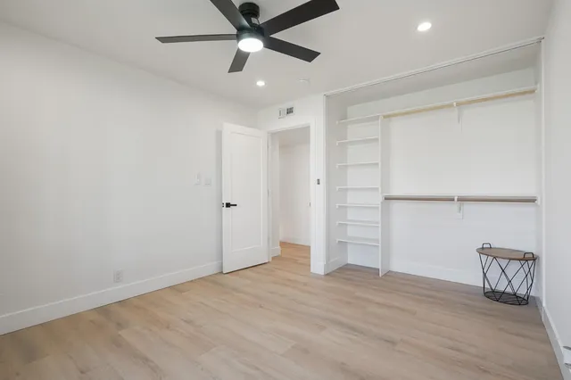 an empty room with wooden floor closet and windows
