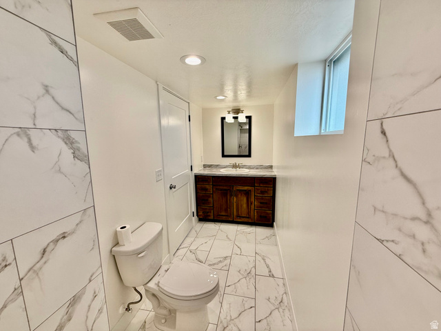 2865 North 3250 W Road Sutherland, UT 84624 - Photo 21 of 28 Bathroom featuring large-format tile flooring and shower surround with marble-look veining, a dark wood-finish vanity with a light-colored countertop, and a contemporary light fixture