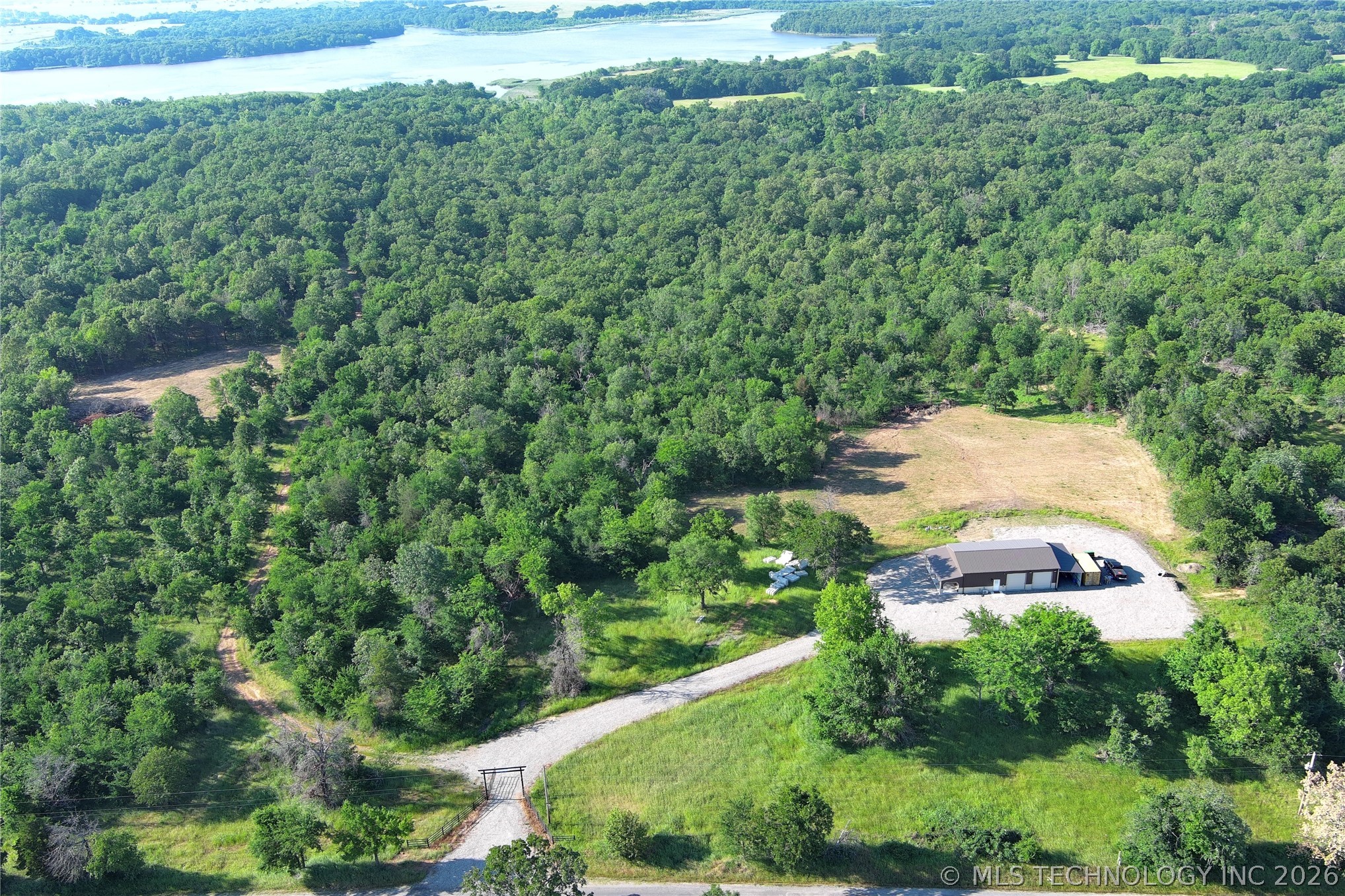 20862 East 1160th Road Keota, OK 74941 - Photo 14 of 47 Expansive wooded acreage featuring a single-story structure with a dark roof and light-colored siding, a gravel driveway, and cleared land surrounding the building