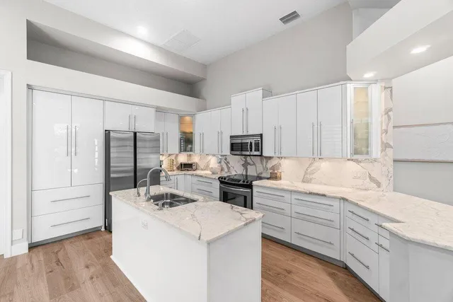 a view of kitchen with stainless steel appliances granite countertop a stove top oven a refrigerator and white cabinets with wooden floor