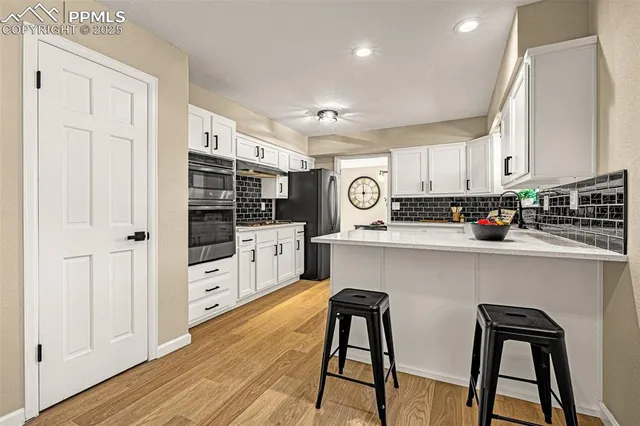 a kitchen with stainless steel appliances a refrigerator a stove a sink dishwasher and white cabinets with wooden floor