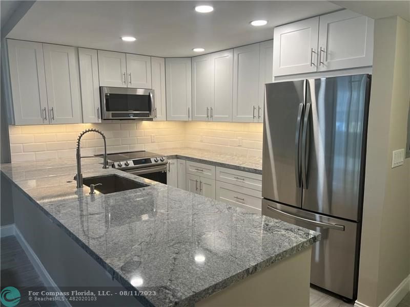 a kitchen with stainless steel appliances granite countertop a refrigerator a stove and a sink with wooden floor