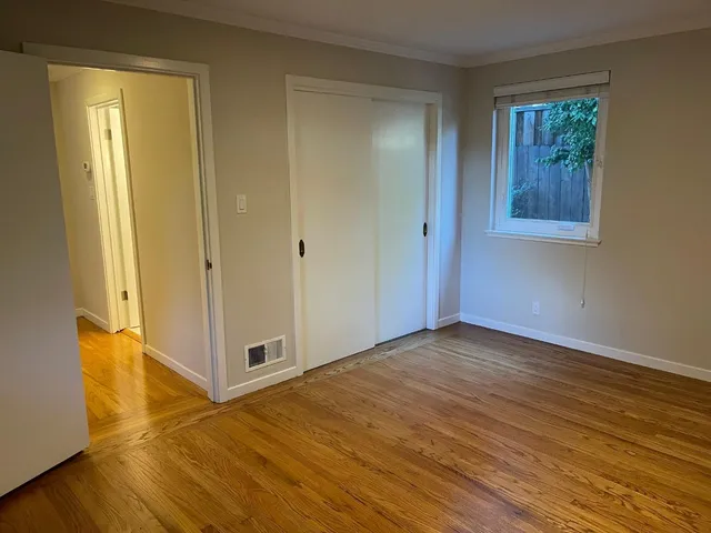a view of an empty room with wooden floor and a window