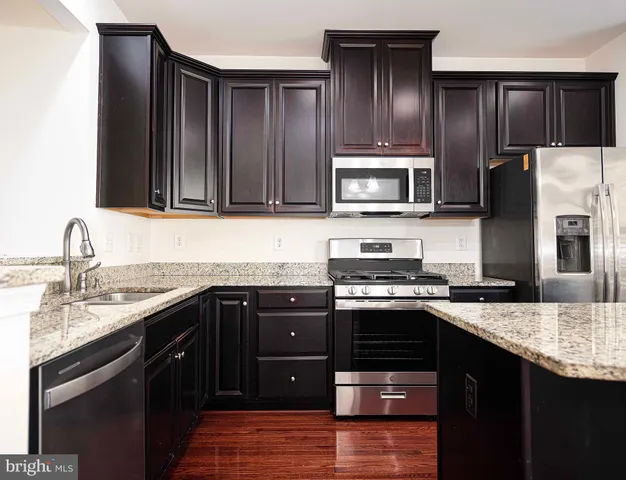 a kitchen with stainless steel appliances granite countertop a refrigerator a stove top oven a sink and dishwasher with wooden floor