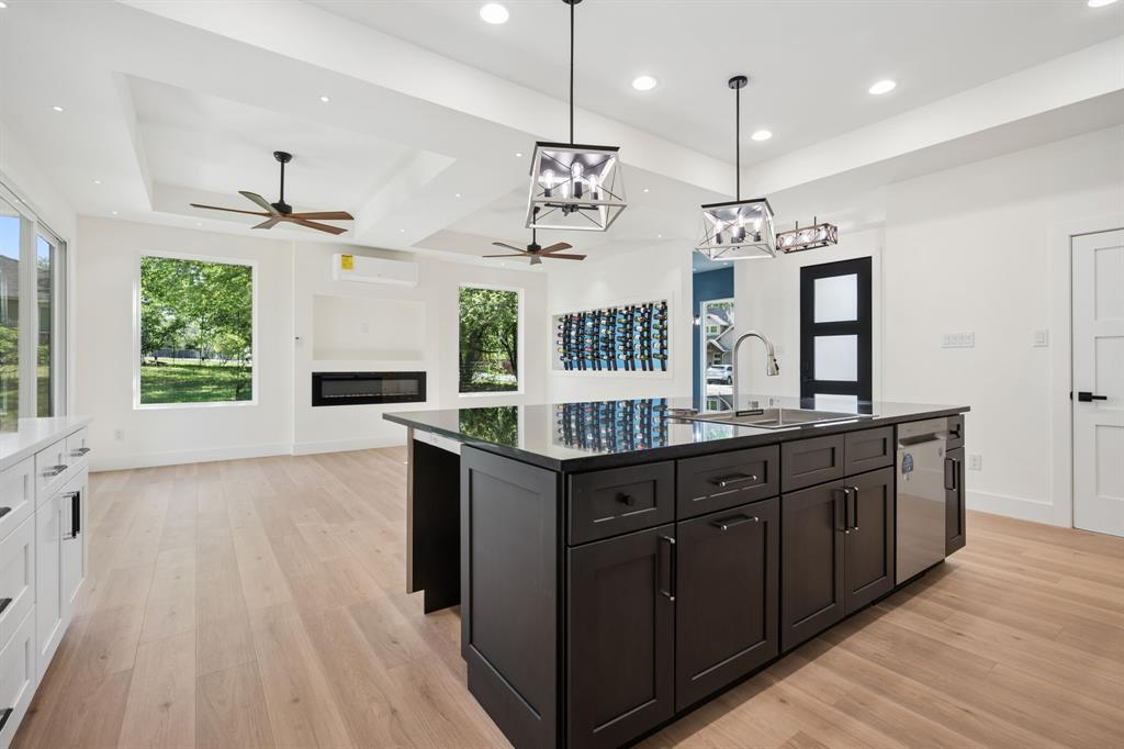 105 Buckboard Trail Oak Point, TX 75068 - Photo 8 of 27 Two tone kitchen with a kitchen island with sink, a glass covered fireplace, light wood finished floors, stainless steel dishwasher, and two tone cabinets. Space for two undercabinet refrigerators.