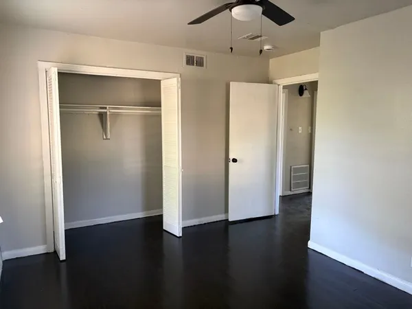 a view of an empty room with wooden floor and a ceiling fan