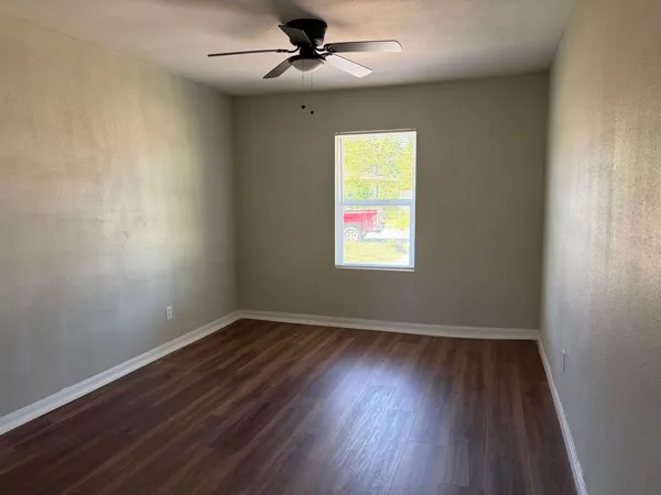 an empty room with wooden floor ceiling fan and windows