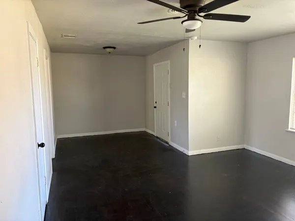 an empty room with wooden floor fan and windows
