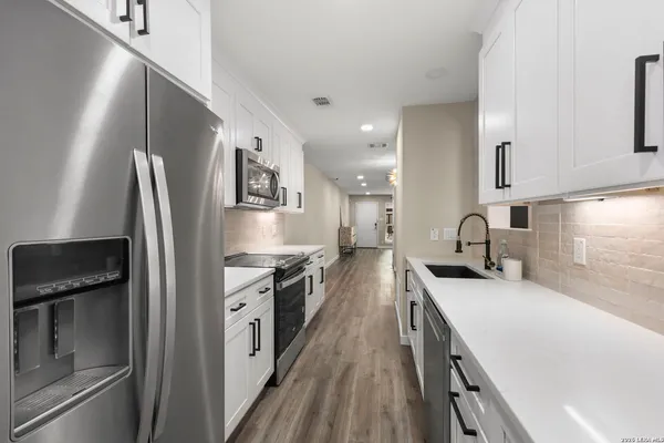 a kitchen with stainless steel appliances granite countertop a refrigerator a stove and a sink with wooden floor