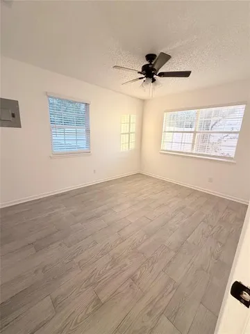 an empty room with wooden floor ceiling fan and windows