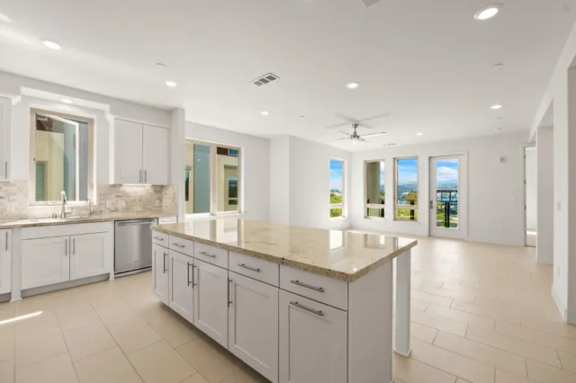 a large white kitchen with granite countertop a sink and dishwasher with a large kitchen island
