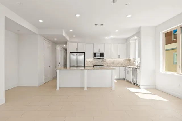 a large white kitchen with kitchen island a sink a center island stainless steel appliances and a window