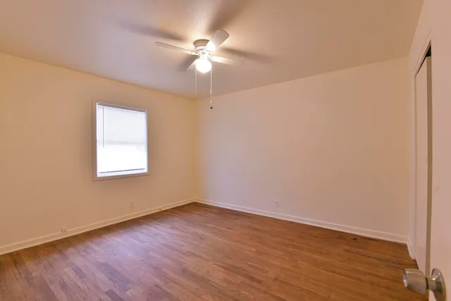 an empty room with wooden floor fan and windows