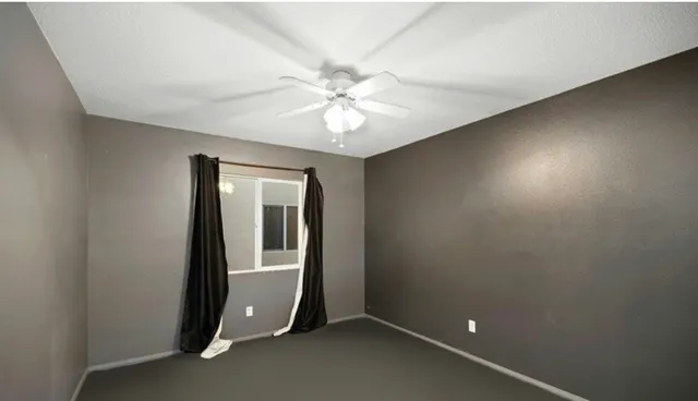 an empty room with chandelier fan and windows