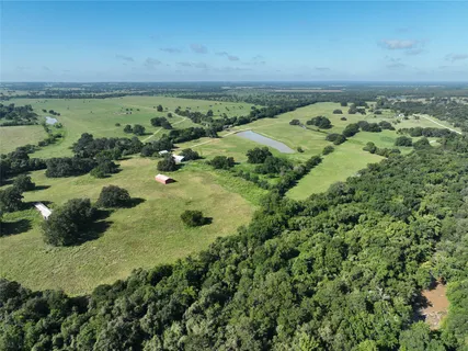 an aerial view of a residential houses with outdoor space and trees all around