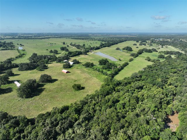 an aerial view of a residential houses with outdoor space and trees all around