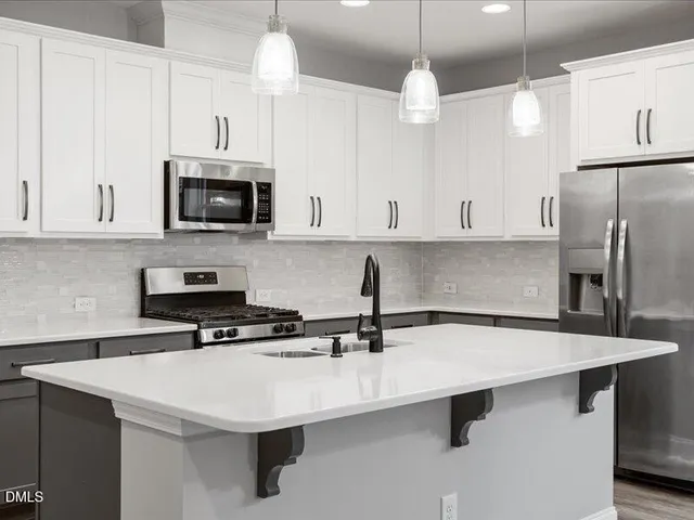 a kitchen with stainless steel appliances a sink a stove a refrigerator a center island and cabinets