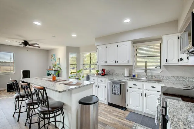 a kitchen that has a lot of cabinets in it with stainless steel appliances granite countertop a stove a refrigerator a stove a sink a dining table and chairs with wooden floor