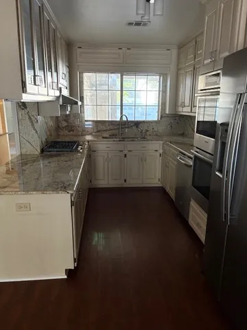 a kitchen with granite countertop a sink a window stainless steel appliances and cabinets