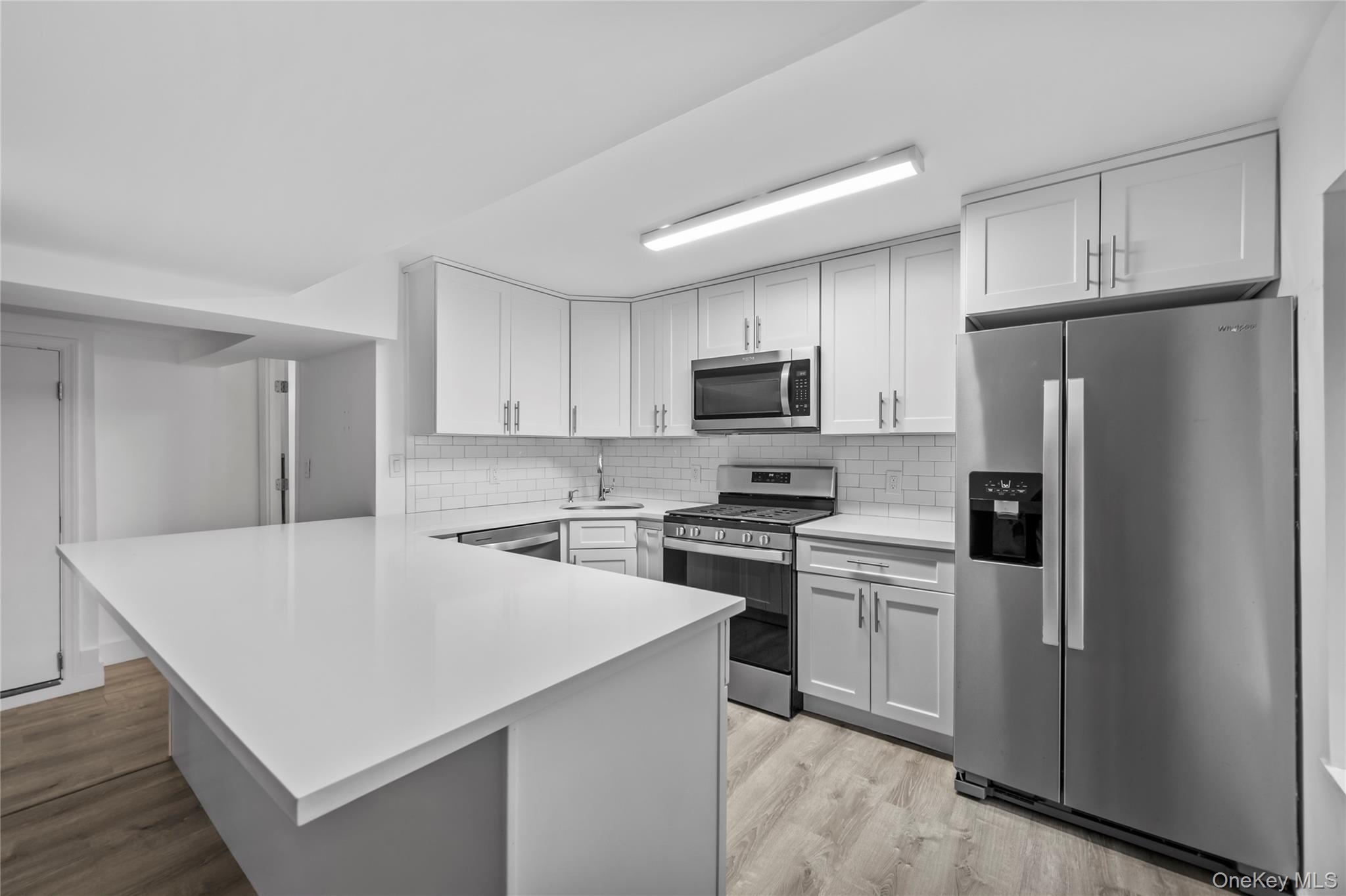 1440 Boston Post Road, Unit 8K Larchmont, NY 10538 - Photo 5 of 20 Kitchen with appliances with stainless steel finishes, a peninsula, light countertops, light wood-type flooring, and backsplash