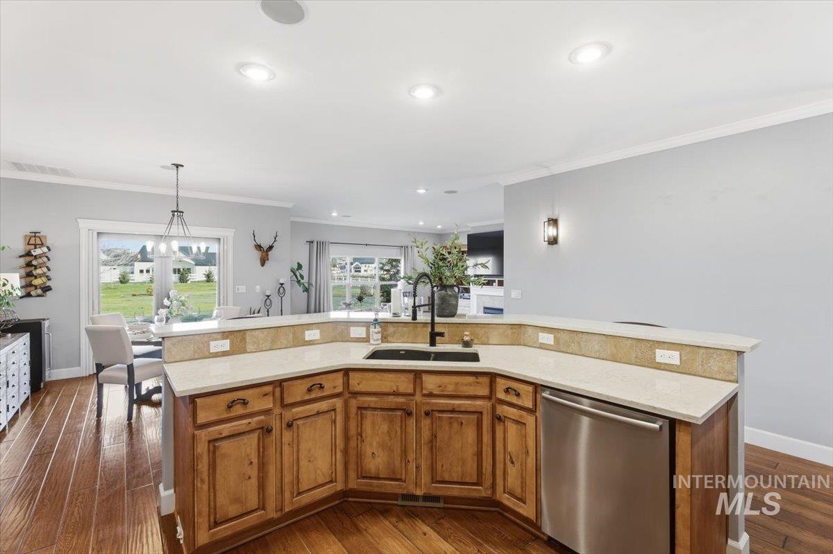 8982 New Castle Drive Middleton, ID 83644 - Photo 13 of 48 Kitchen with brown cabinetry, dishwasher, crown molding, a kitchen island with sink, and hanging light fixtures