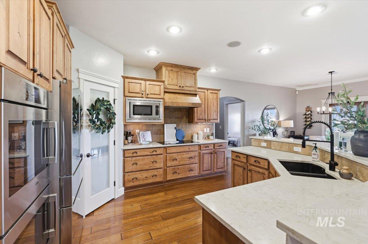 8982 New Castle Drive Middleton, ID 83644 - Photo 16 of 48 Kitchen with stainless steel appliances, decorative light fixtures, dark wood finished floors, decorative backsplash, and a kitchen island with sink