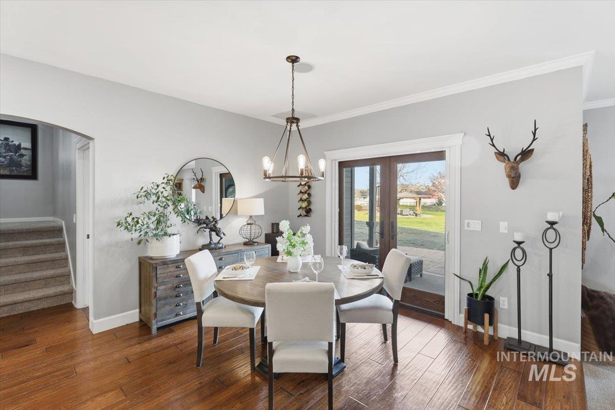8982 New Castle Drive Middleton, ID 83644 - Photo 17 of 48 Dining room with stairway, dark wood-style floors, arched walkways, a chandelier, and crown molding