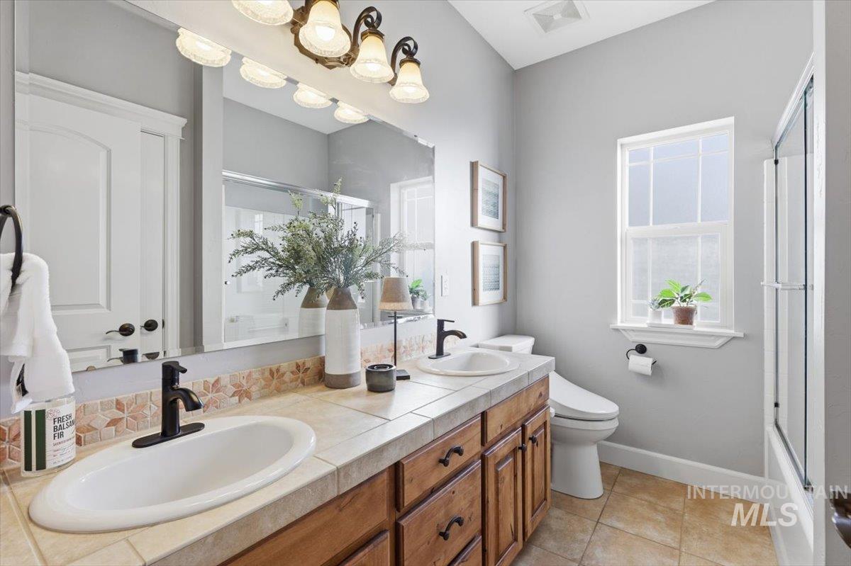 8982 New Castle Drive Middleton, ID 83644 - Photo 9 of 48 Full bath with double vanity, light tile patterned flooring, bath / shower combo with glass door, and decorative backsplash