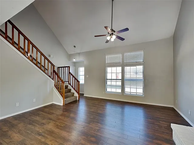a view of an empty room with wooden floor ceiling fan and windows