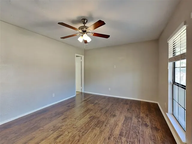 an empty room with wooden floor fan and windows