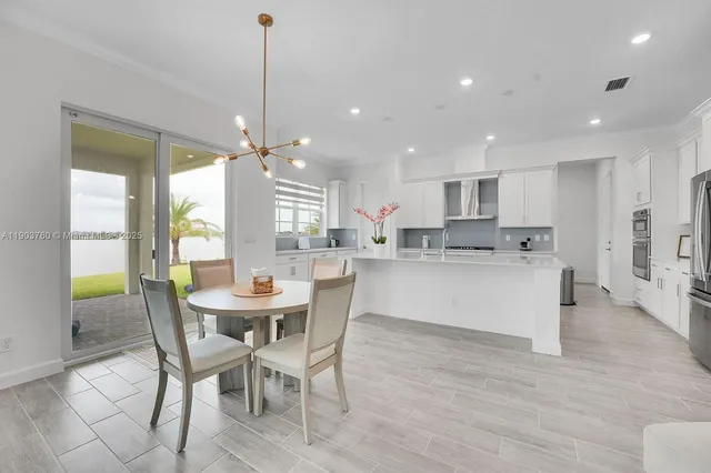 a kitchen with stainless steel appliances kitchen island granite countertop a dining table chairs and white cabinets