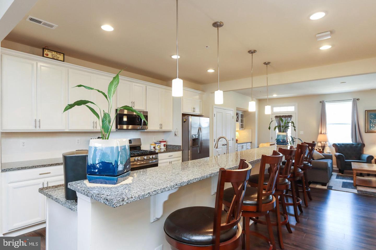 7146 Proclamation Place Frederick, MD 21703 - Photo 7 of 26 a kitchen with stainless steel appliances granite countertop a stove a refrigerator a sink a dining table and chairs with wooden floor