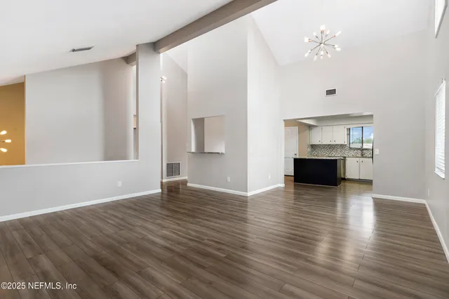 a view of empty room with wooden floor and kitchen view