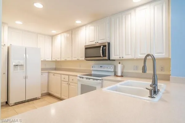 a kitchen with stainless steel appliances granite countertop a refrigerator a stove a sink and white cabinets with wooden floor