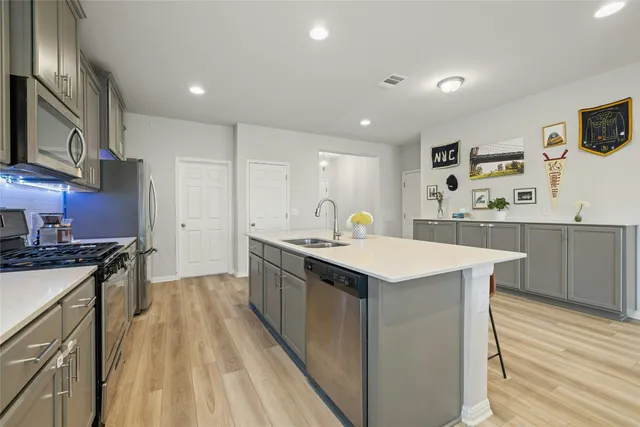 a kitchen with stainless steel appliances granite countertop a sink a stove a refrigerator and white cabinets with wooden floor