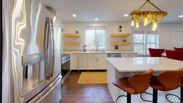 a kitchen with stainless steel appliances granite countertop a refrigerator a sink dishwasher a stove and a dining table with wooden floor