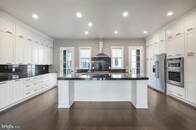 a kitchen with stainless steel appliances granite countertop a stove a sink and white cabinets with wooden floor