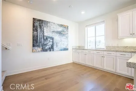 a large white kitchen with granite countertop a stove a sink and a granite countertops with wooden floor