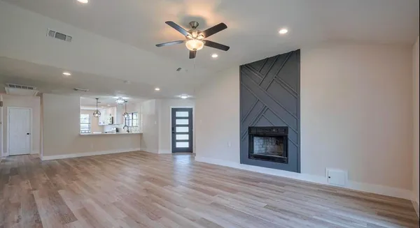 an empty room with large windows a fireplace a ceiling fan and wooden floor