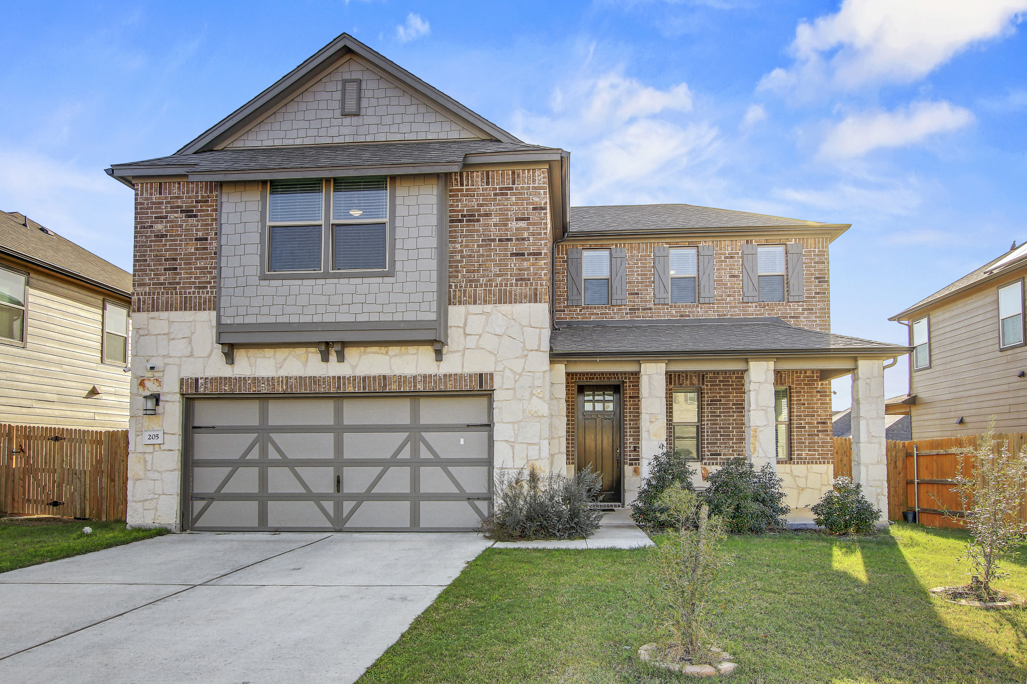 Craftsman-style house featuring a garage, stone siding, driveway, and brick siding
