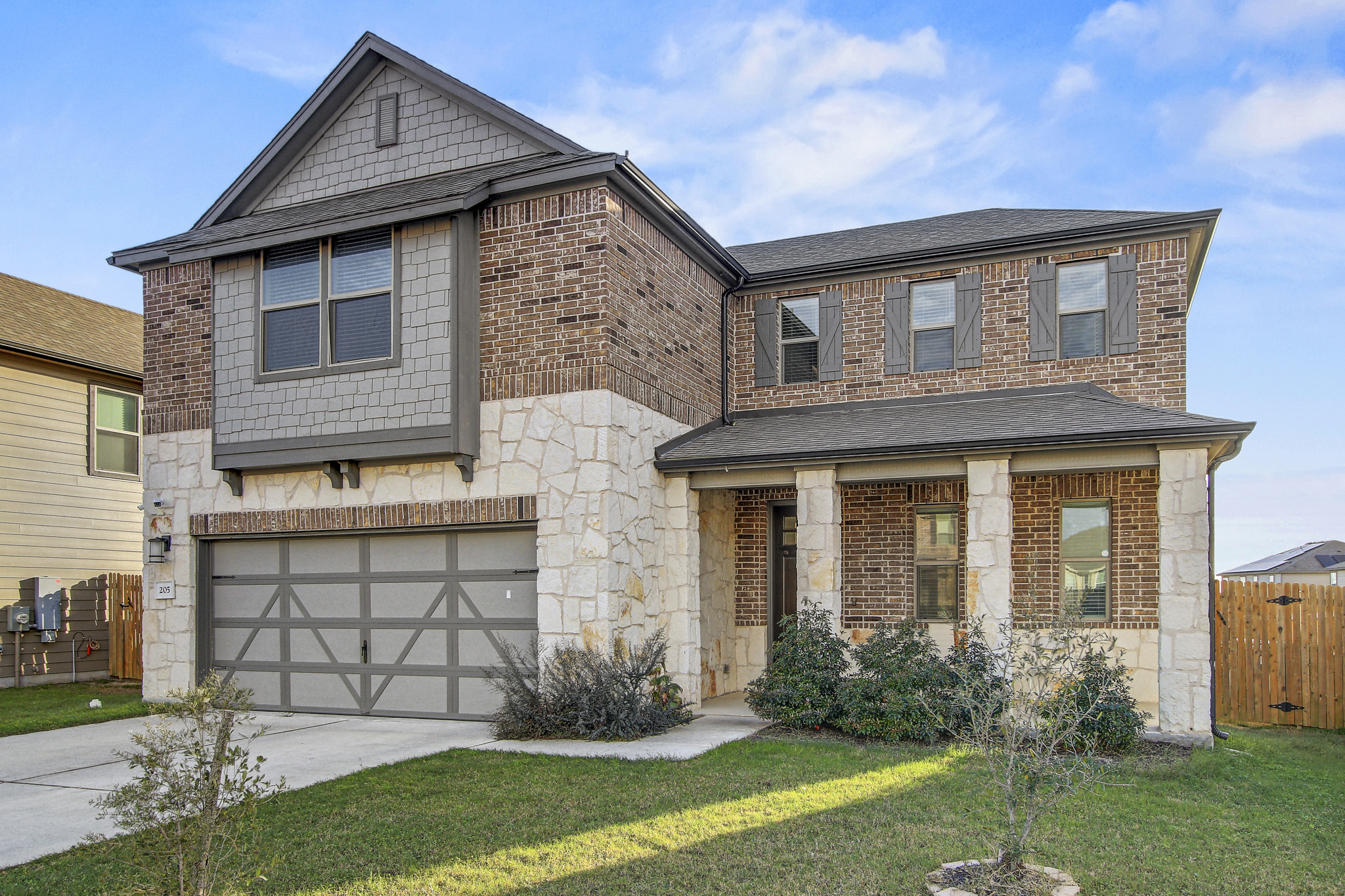 205 Travers Stake Trail Elgin, TX 78621 - Photo 2 of 28 View of front of property with a garage, concrete driveway, covered porch, brick siding, and stone siding