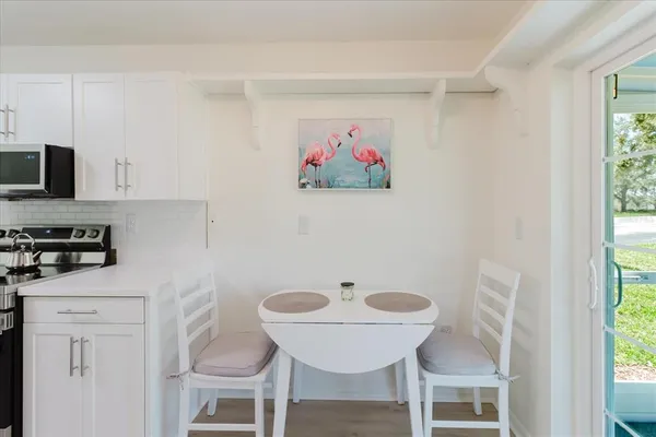 a kitchen with stainless steel appliances a white refrigerator a sink a stove a dining table and chairs with wooden floor