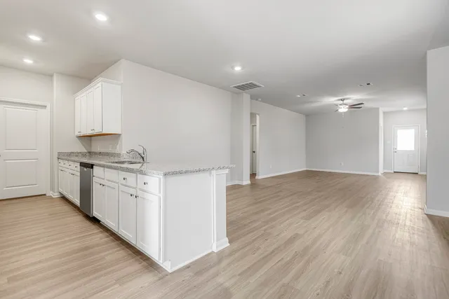 a kitchen with granite countertop a stove top oven a sink and white cabinets with wooden floor