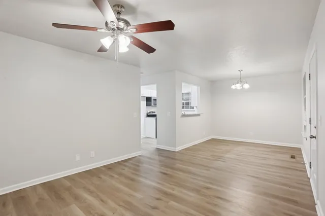 an empty room with wooden floor chandelier fan and windows