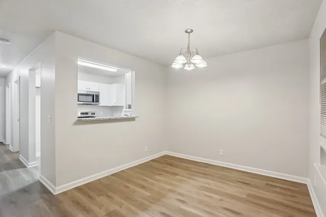 an empty room with wooden floor and kitchen view