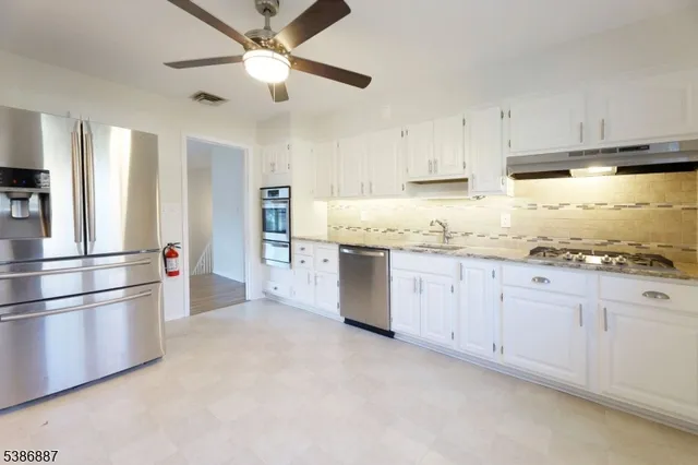 a kitchen with granite countertop a refrigerator a sink and white cabinets
