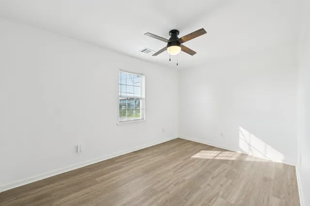 an empty room with wooden floor fan and windows