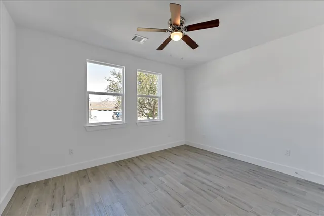an empty room with wooden floor fan and windows