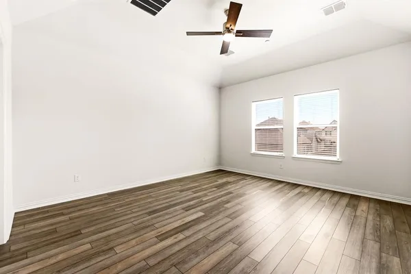 an empty room with wooden floor fan and windows