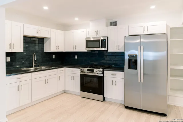 a kitchen with stainless steel appliances granite countertop a refrigerator a stove a sink and white cabinets
